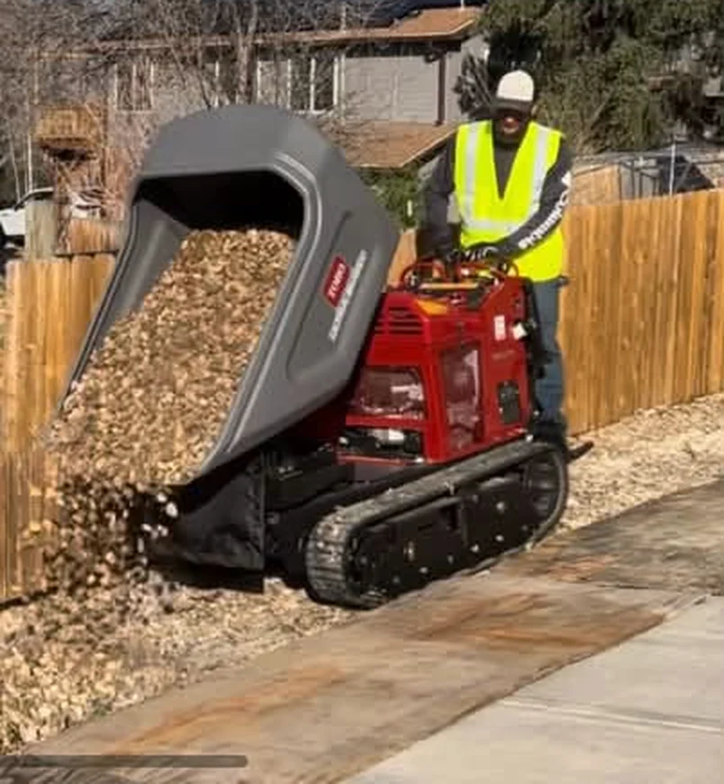 Outdoor Legacy worker using a compact tracked material carrier to place decorative rock beside a concrete residential access lane